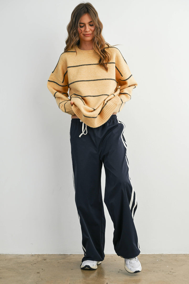 Woman in cozy mustard sweater with black stripes, navy track pants, and white sneakers for casual PNW style