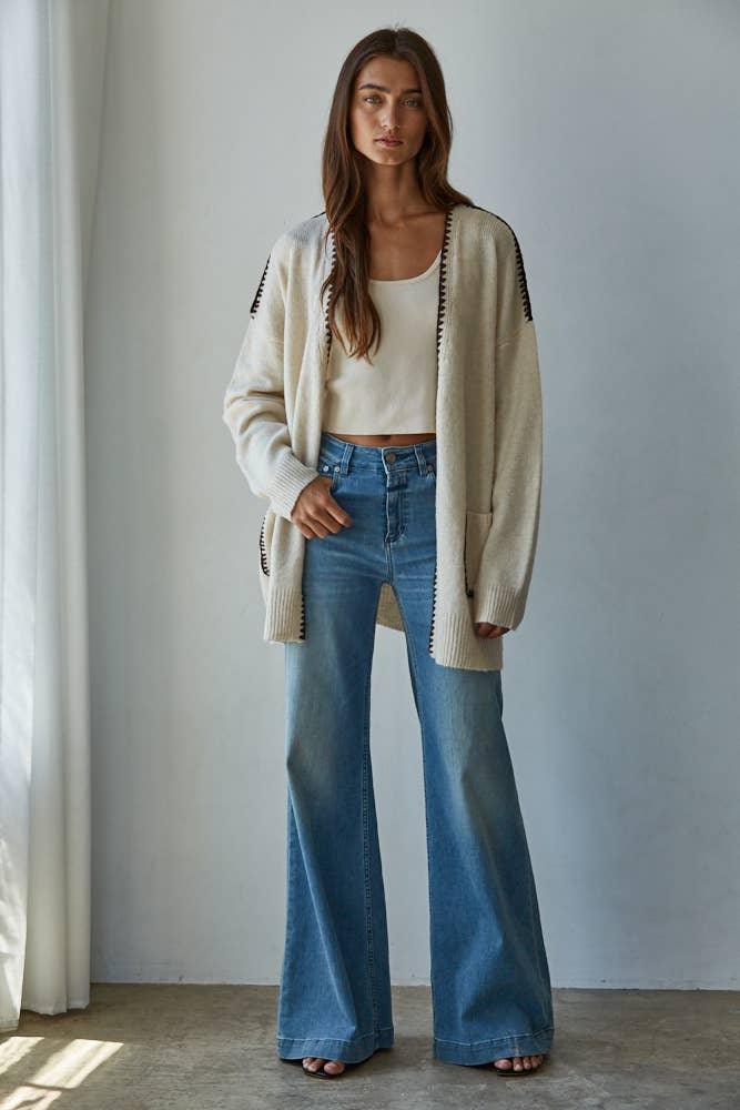 Woman in cozy cream cardigan, white crop top, and wide-leg denim jeans for coastal PNW style