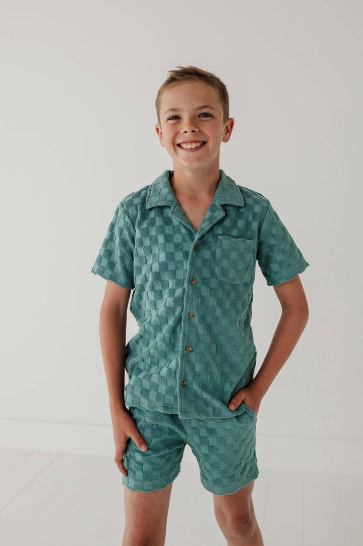 Boy in teal checkered short sleeve pajama set with button front and shorts, cozy coastal style sleepwear