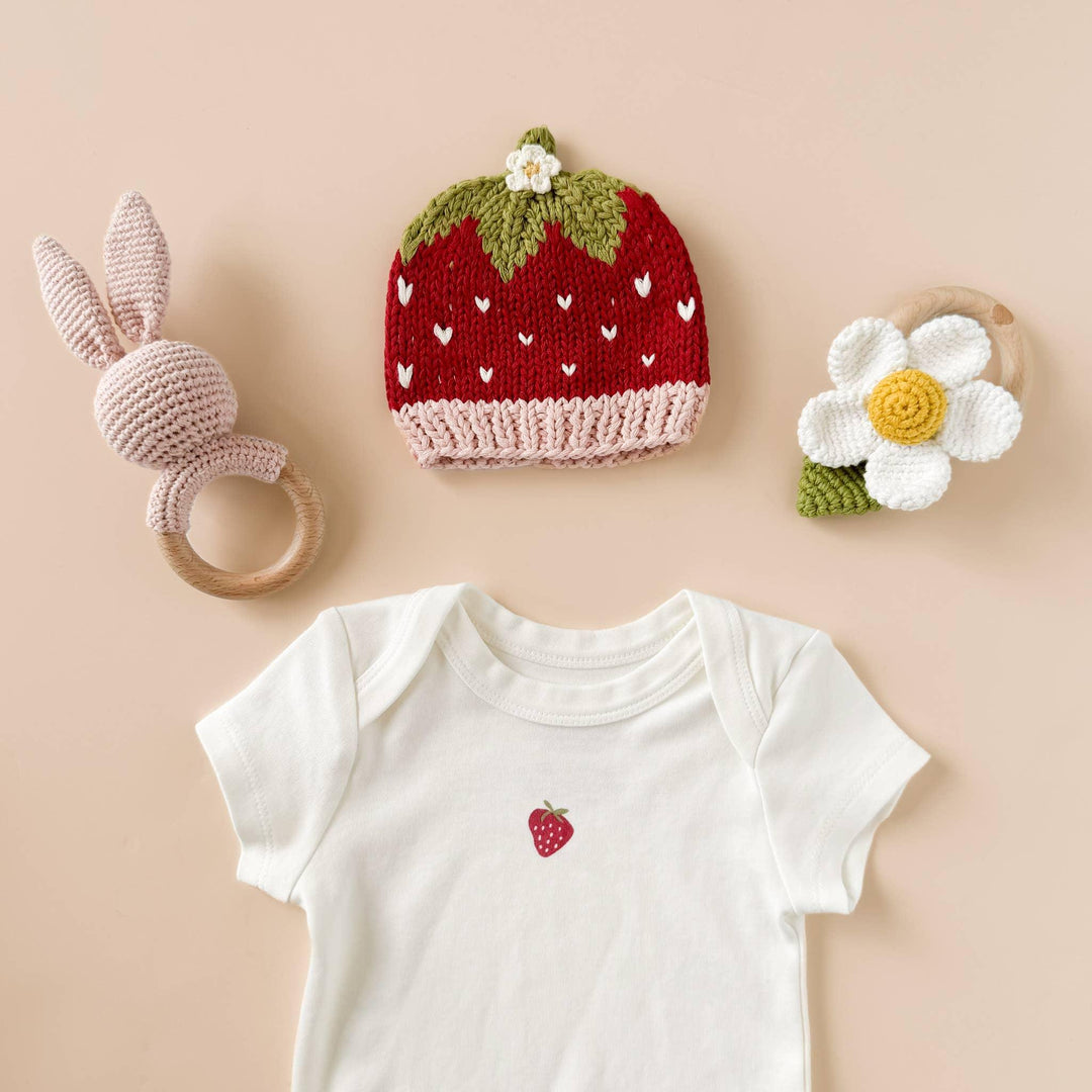 Strawberry knit hat, bunny rattle, daisy teether, and baby onesie with strawberry print