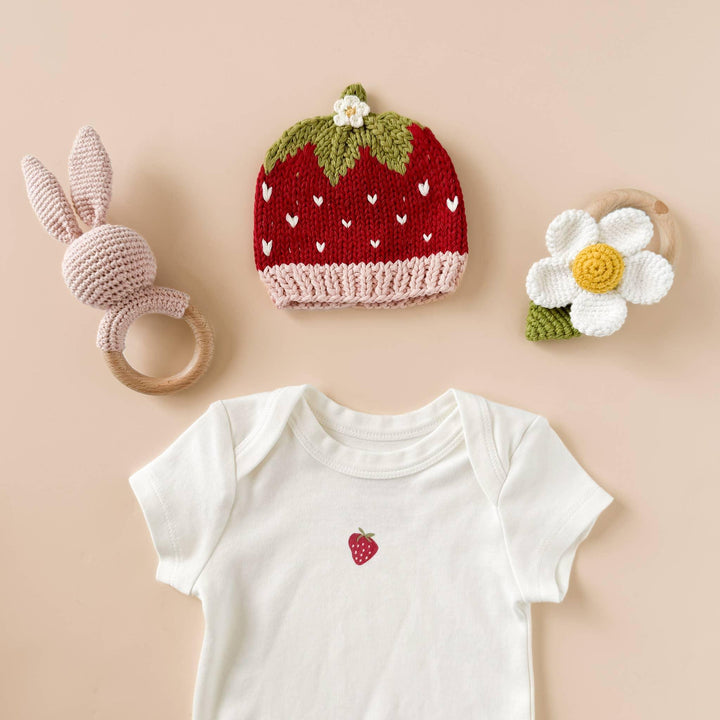 Strawberry knit hat, bunny rattle, daisy teether, and baby onesie with strawberry print