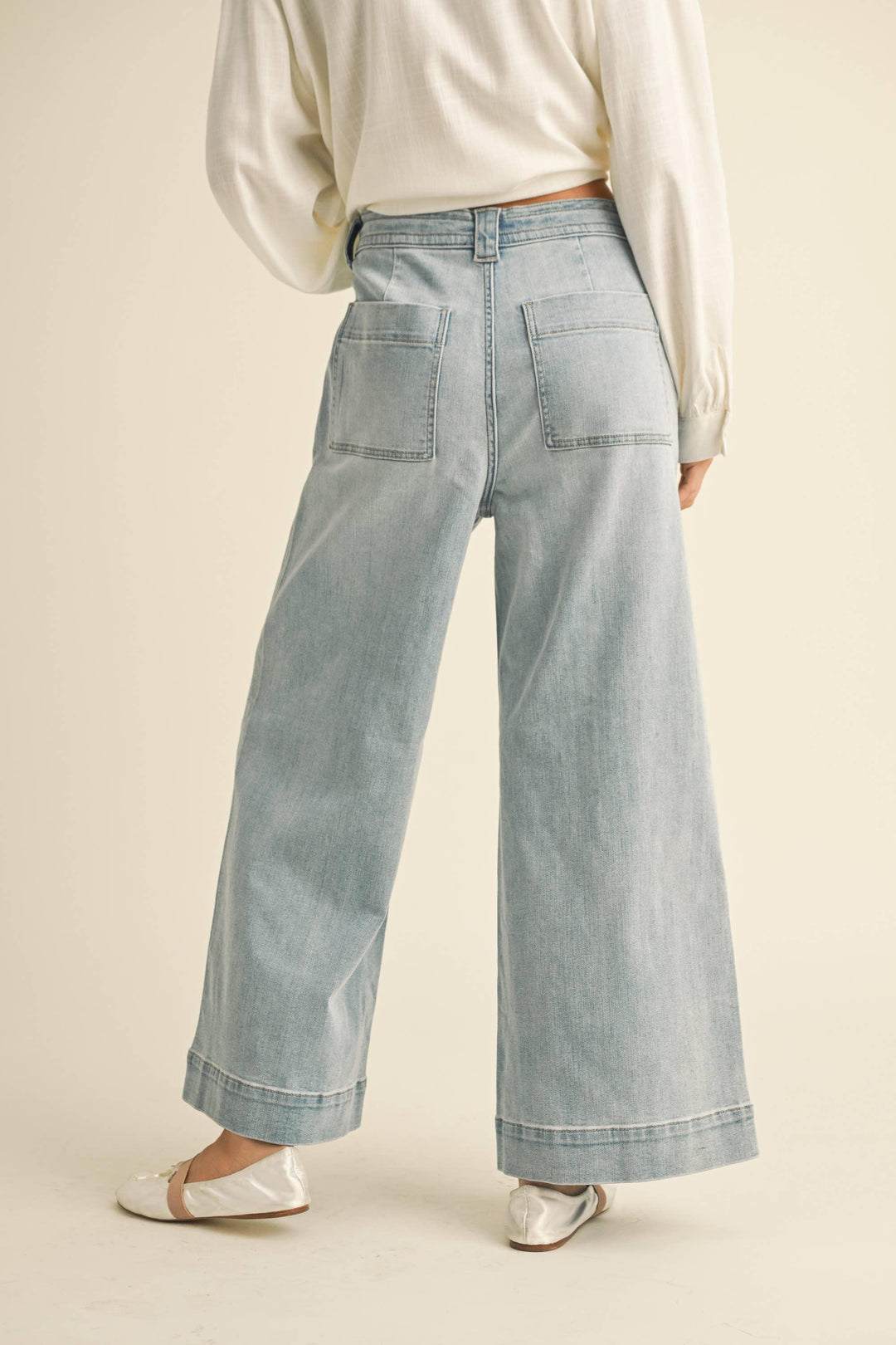 Light wash wide-leg denim jeans with back pockets, paired with cream blouse and white flats