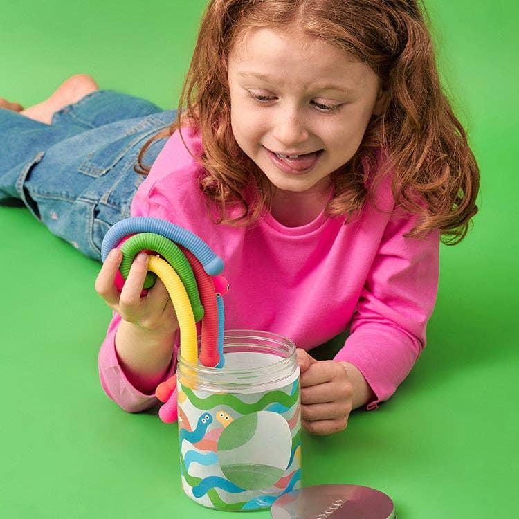 Child playing with colorful bendy straws and a fun patterned cup on green background