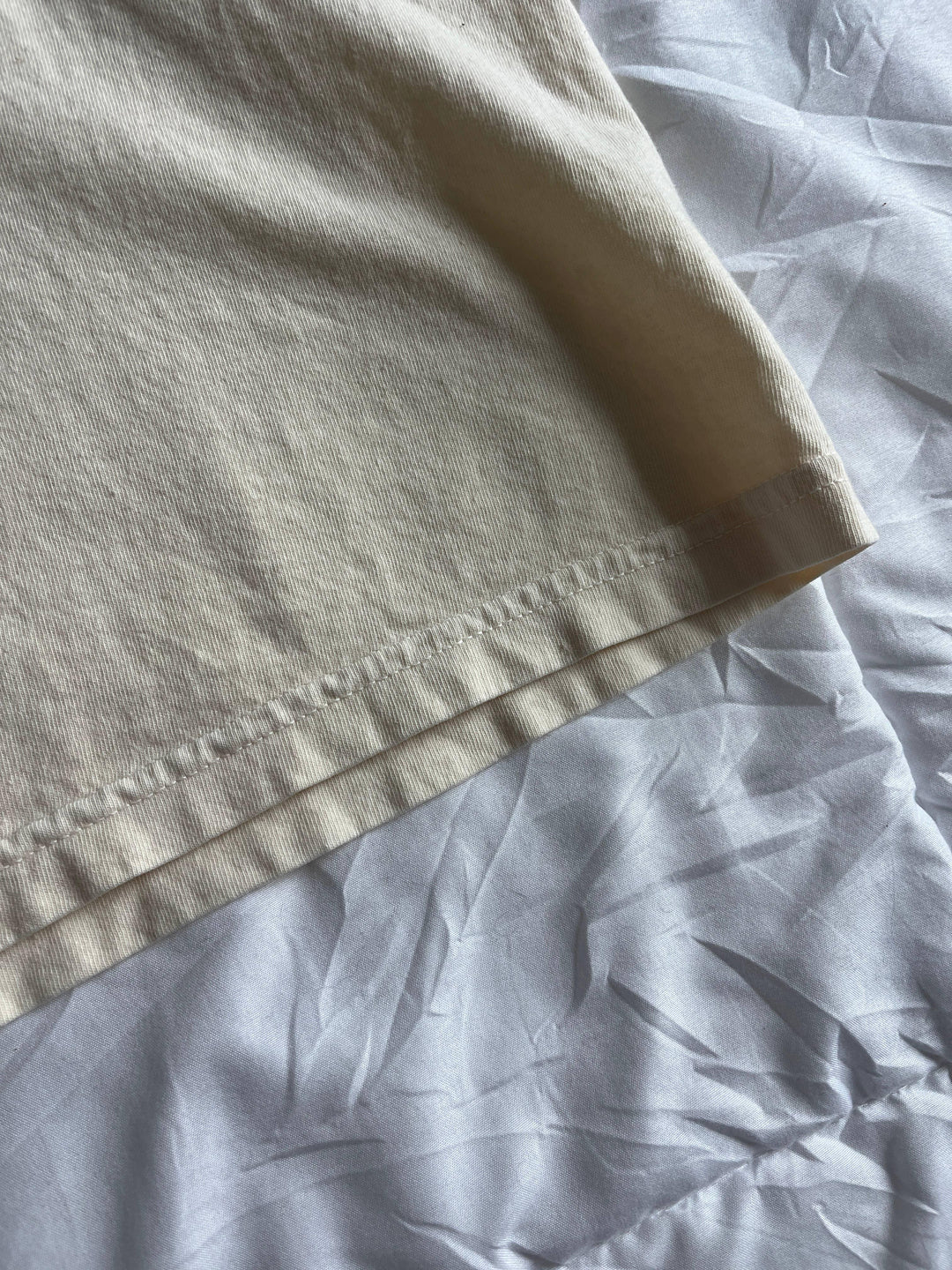 Close-up of beige t-shirt sleeve hem on light gray fabric, showcasing soft cotton texture and clean stitching for everyday coastal style.