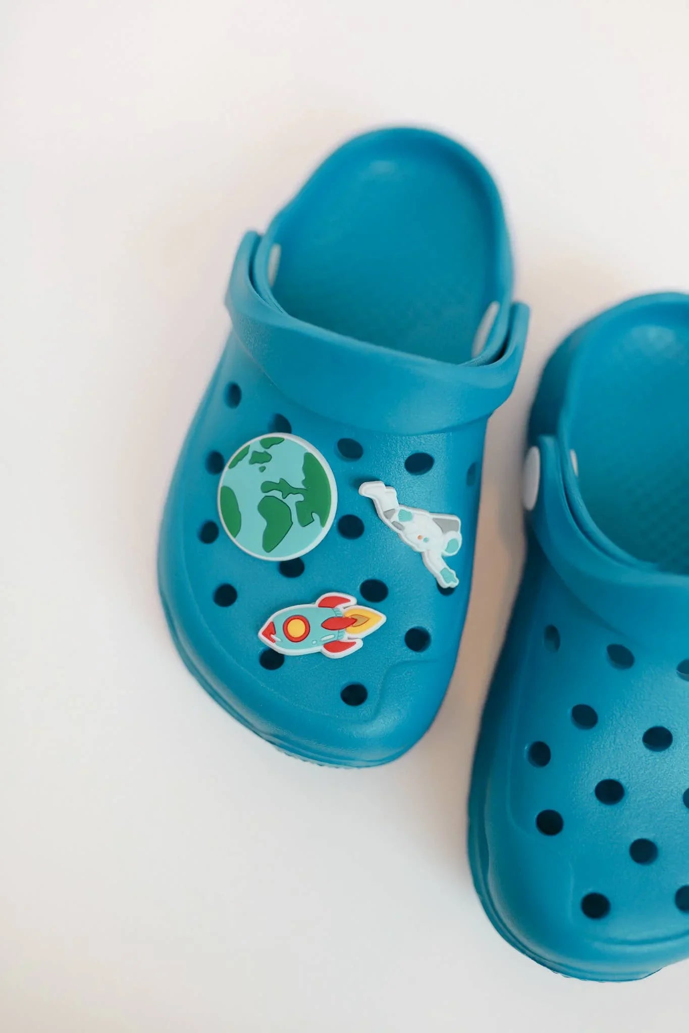 Blue kids' clogs with space-themed Jibbitz charms: rocket, astronaut, Earth — perfect for coastal adventures.