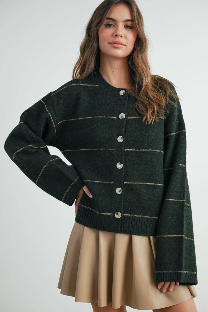 Dark green button-up cardigan with gold stripes, styled with tan pleated skirt for cozy coastal fashion.