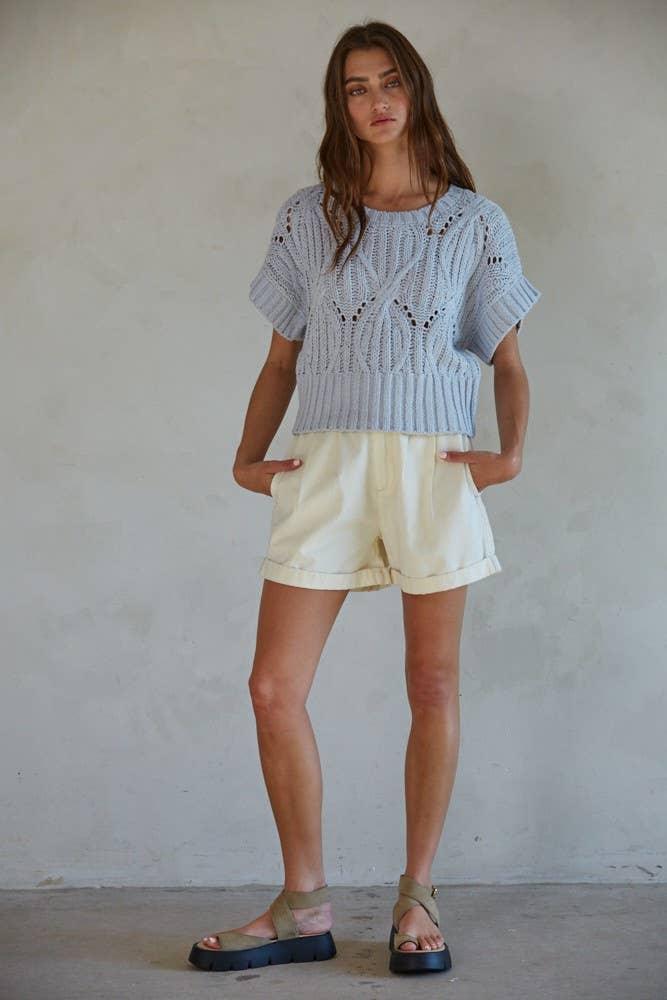Woman in light blue knit crop top and cream shorts, casual summer outfit