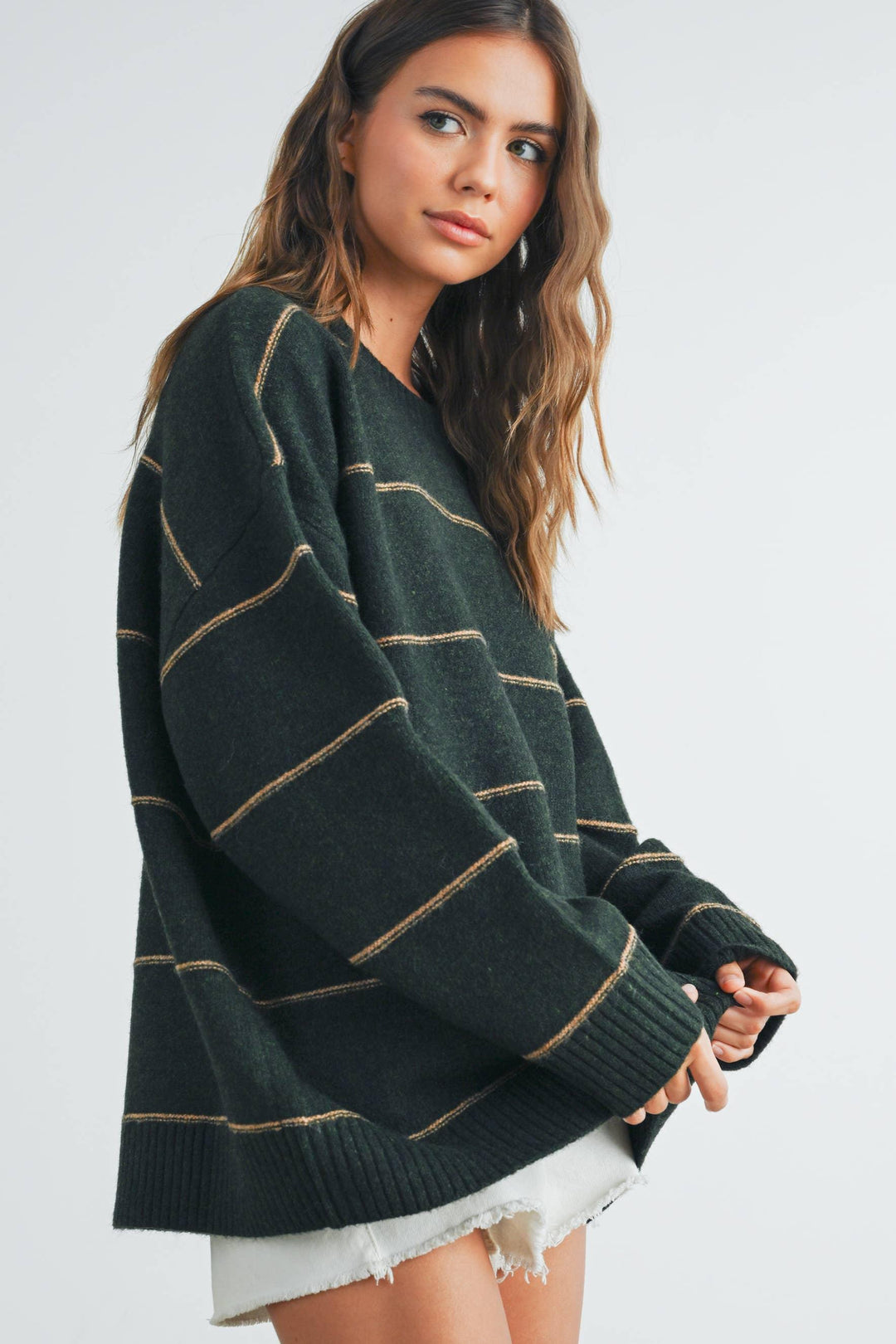 Woman wearing cozy green striped sweater with ribbed cuffs, styled with white denim shorts.