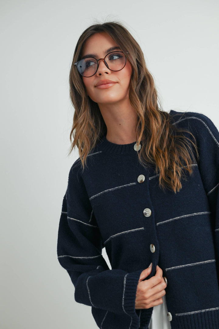 Woman in navy knit cardigan with white stripes and buttons, coastal style outfit