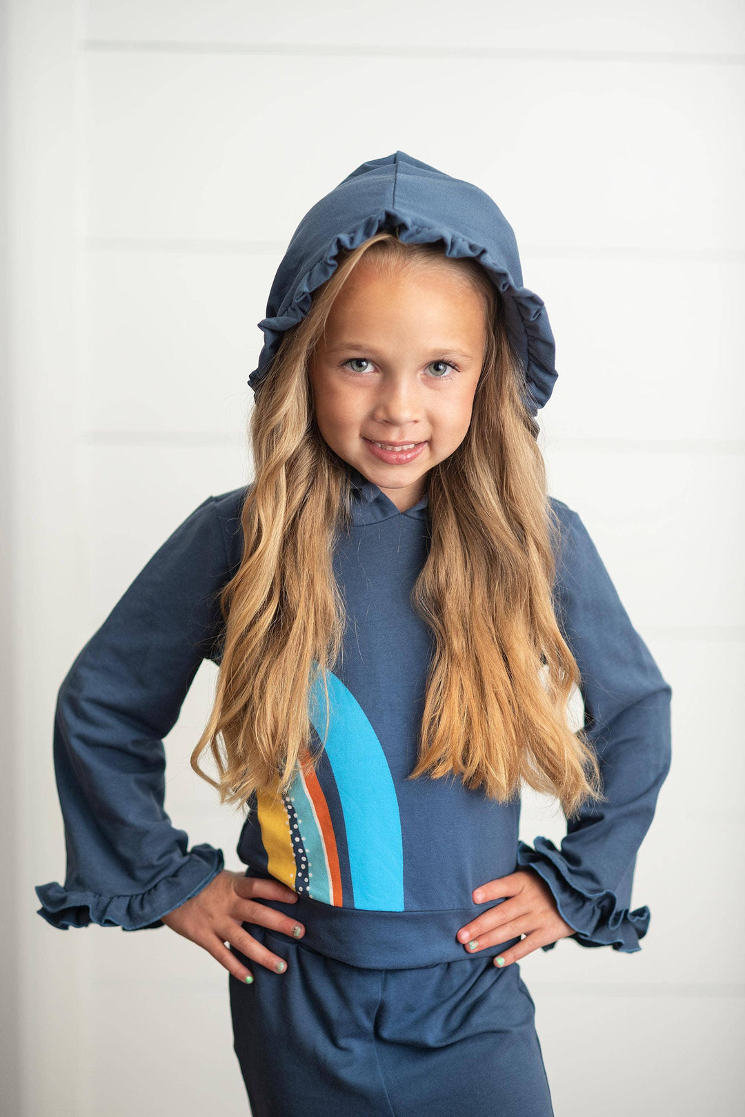 Girl in navy blue ruffled hooded sweatshirt with colorful surfboard graphic, coastal style kids apparel