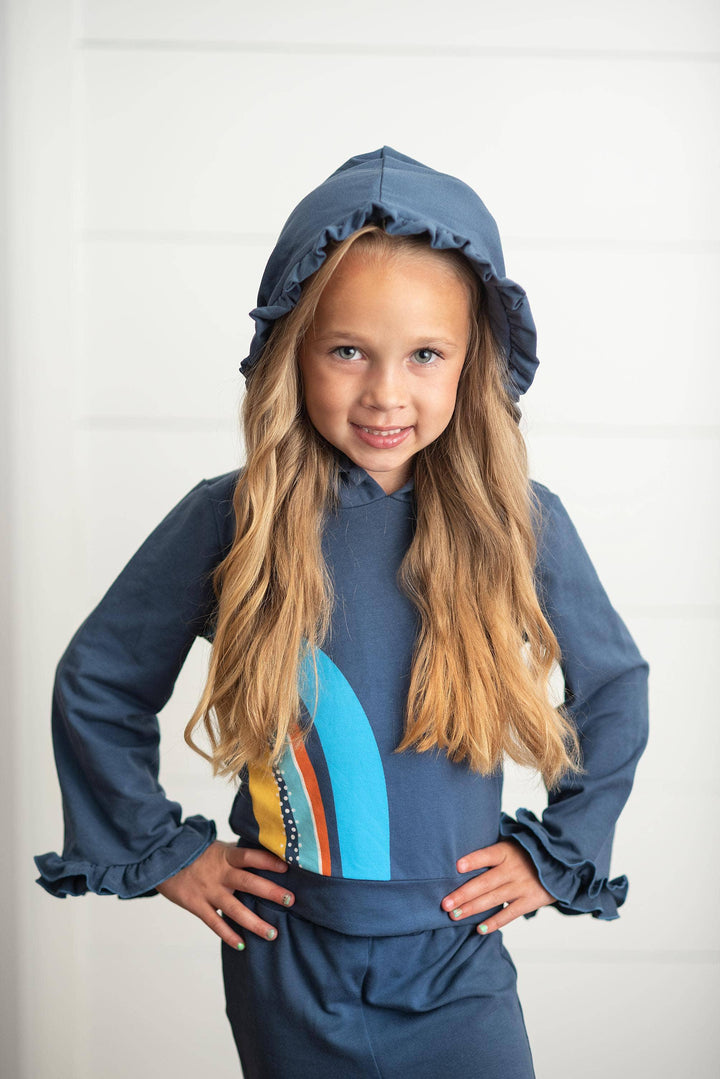 Girl in navy blue ruffled hooded sweatshirt with colorful surfboard graphic, coastal style kids apparel