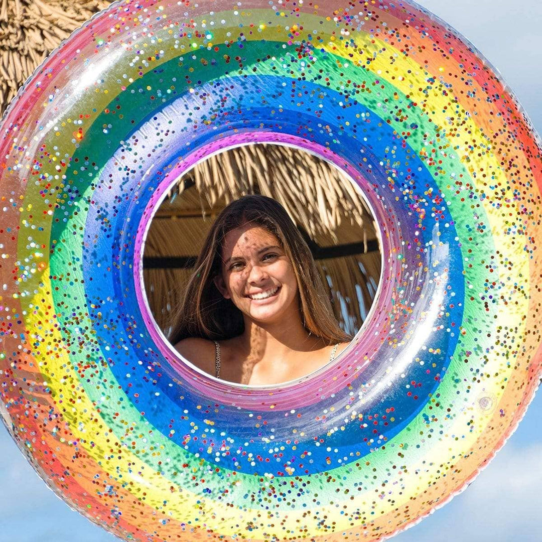 Rainbow glitter pool float with woman smiling through center, beach vibes