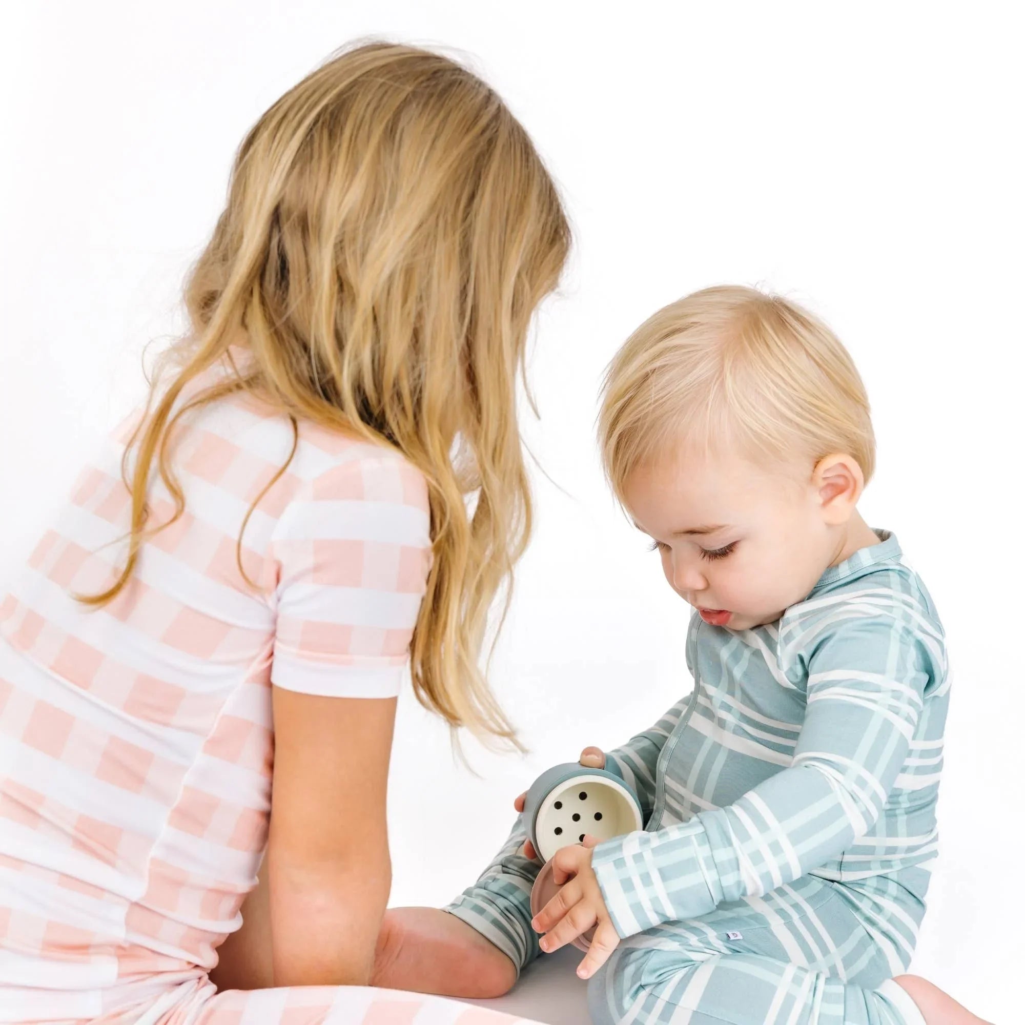 Toddler in blue plaid pajamas playing with toy, girl in pink gingham pajamas nearby