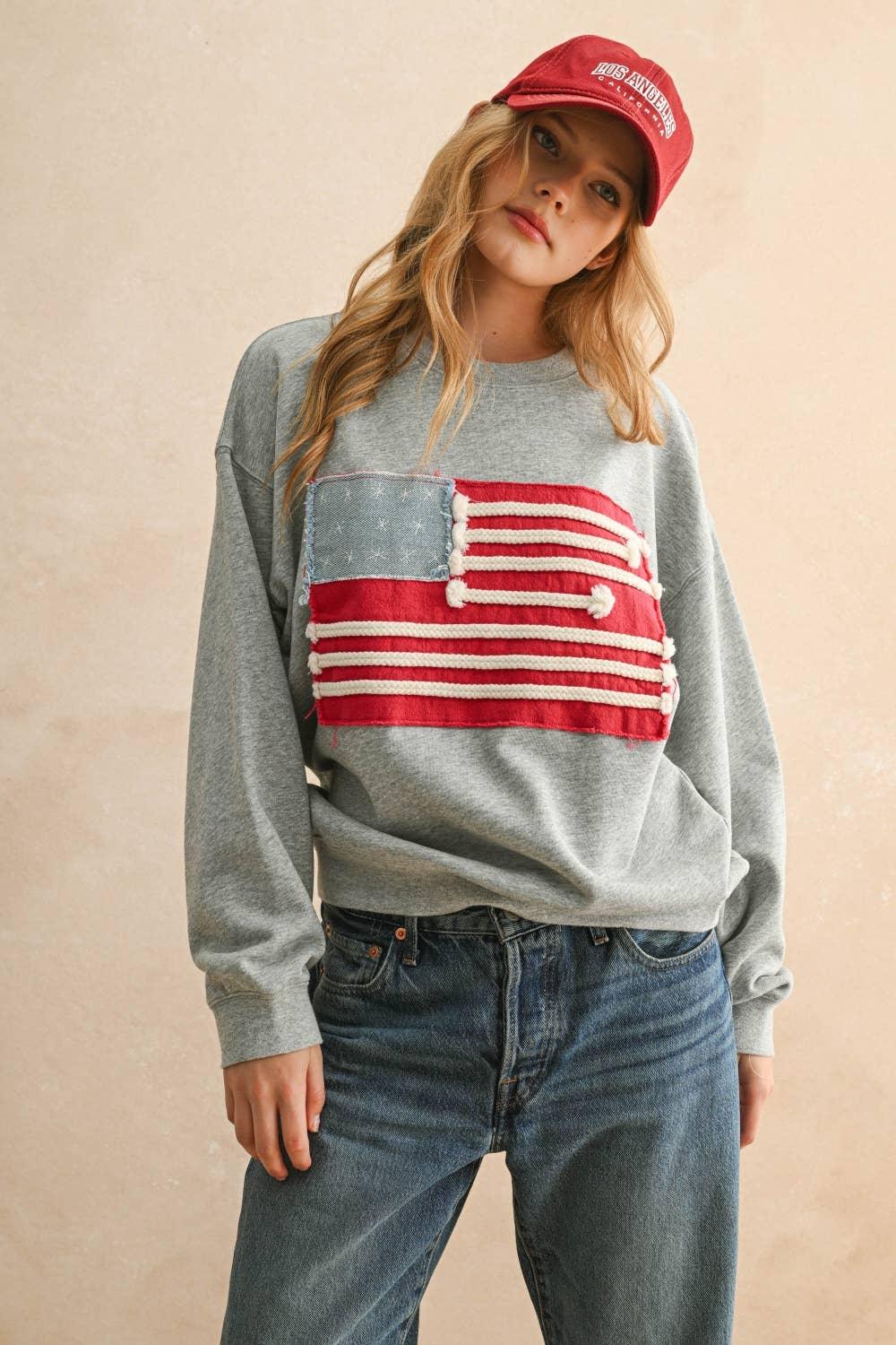 Woman wearing a grey Miou Muse sweatshirt with a red and white flag patch and a red cap.