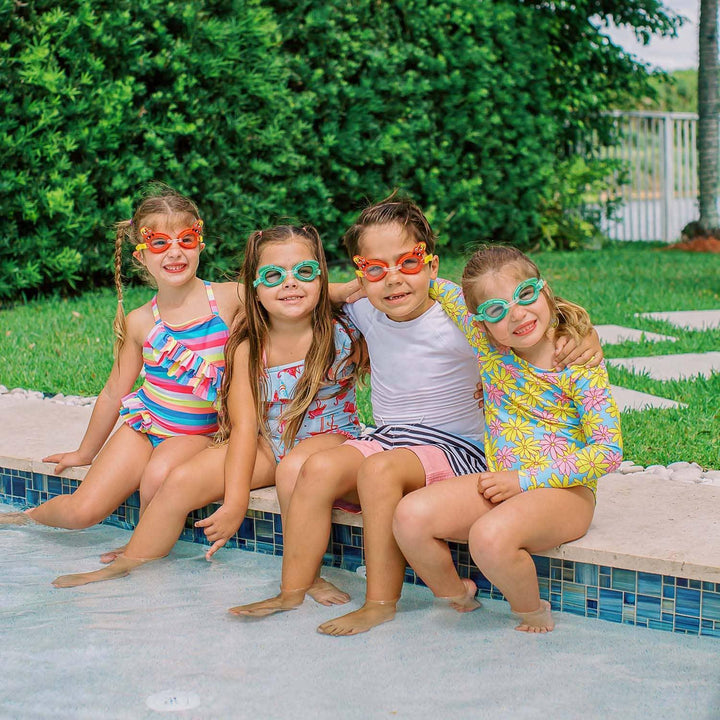 Four children wearing colorful PoolCandy swim goggles sitting by a swimming pool.