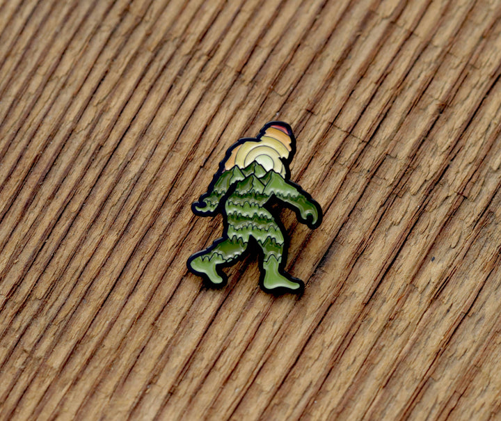 Green mountain-themed enamel pin on wooden surface