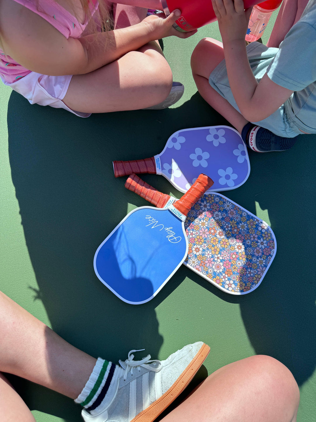 Kids enjoying outdoor fun with colorful pickleball paddles and water bottles on a sunny court