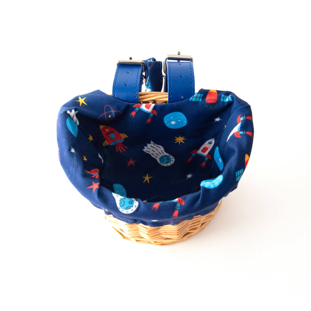 Woven bike basket with space-themed liner featuring rockets, planets, and stars for outdoor adventures.