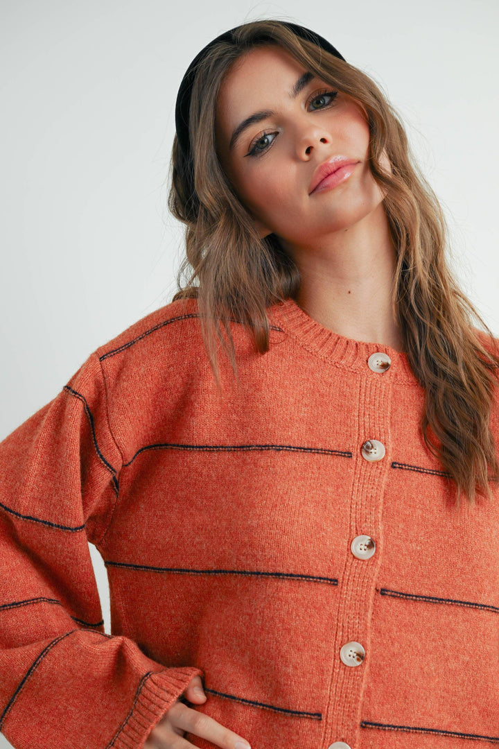 Woman in cozy orange knit cardigan with contrast stitching and buttons, styled with black headband for PNW coastal look
