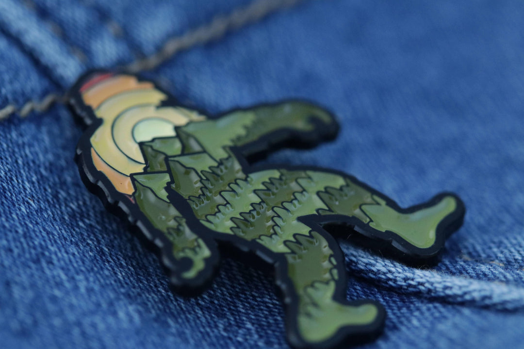 Green dinosaur enamel pin on denim, featuring sunset design and textured scales