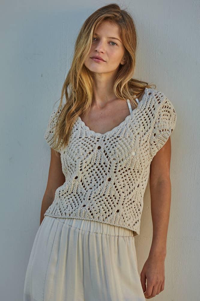 Woman wearing cream crochet knit top with lace pattern, short sleeves, and V-neck, paired with white skirt
