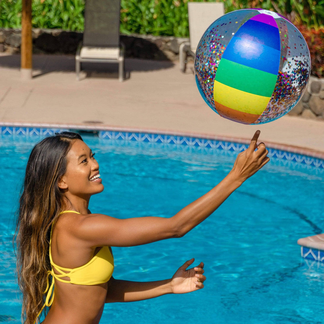 Woman in yellow bikini playing with rainbow confetti beach ball by pool, perfect for summer fun and outdoor adventures.