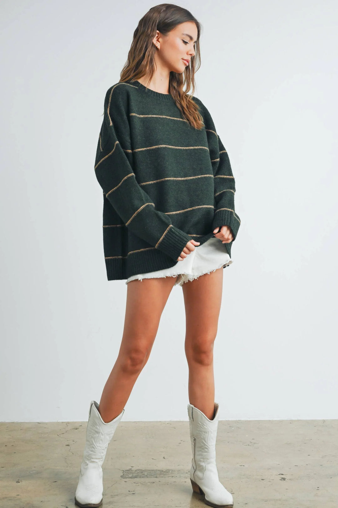 Woman in oversized green striped sweater, white denim shorts, and white cowboy boots