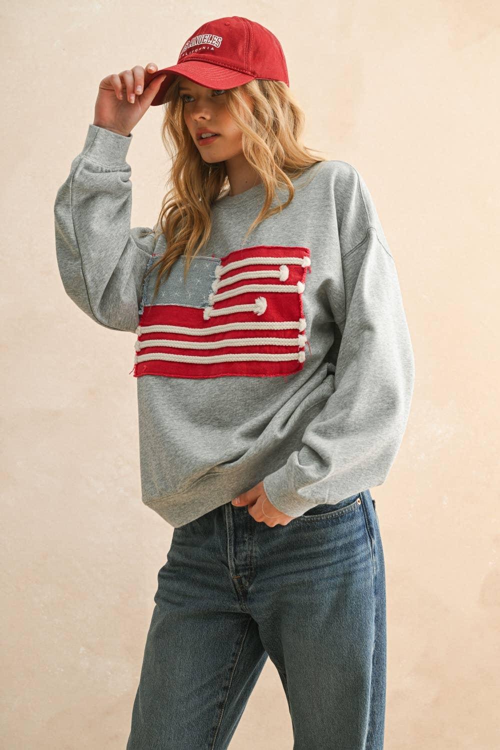 Woman wearing a grey Miou Muse sweatshirt with a red flag patch and a red baseball cap.