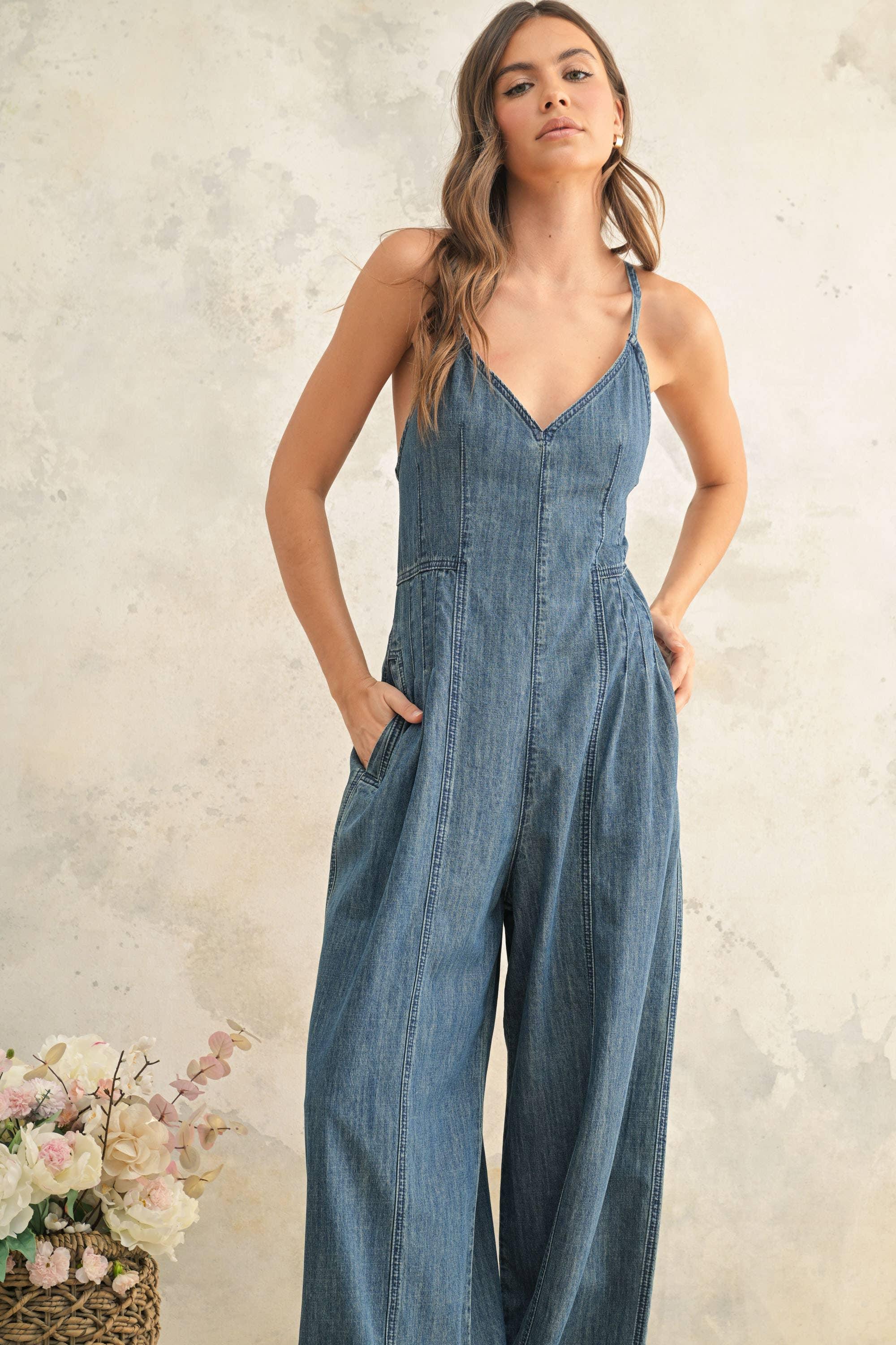 Woman in denim jumpsuit with wide legs and V-neck, hands in pockets, beside floral basket