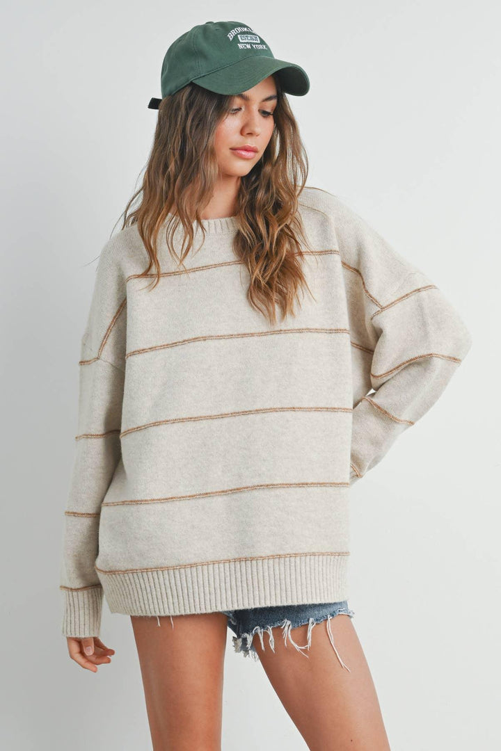 Oversized striped sweater with ribbed hem, paired with denim shorts and a green baseball cap.