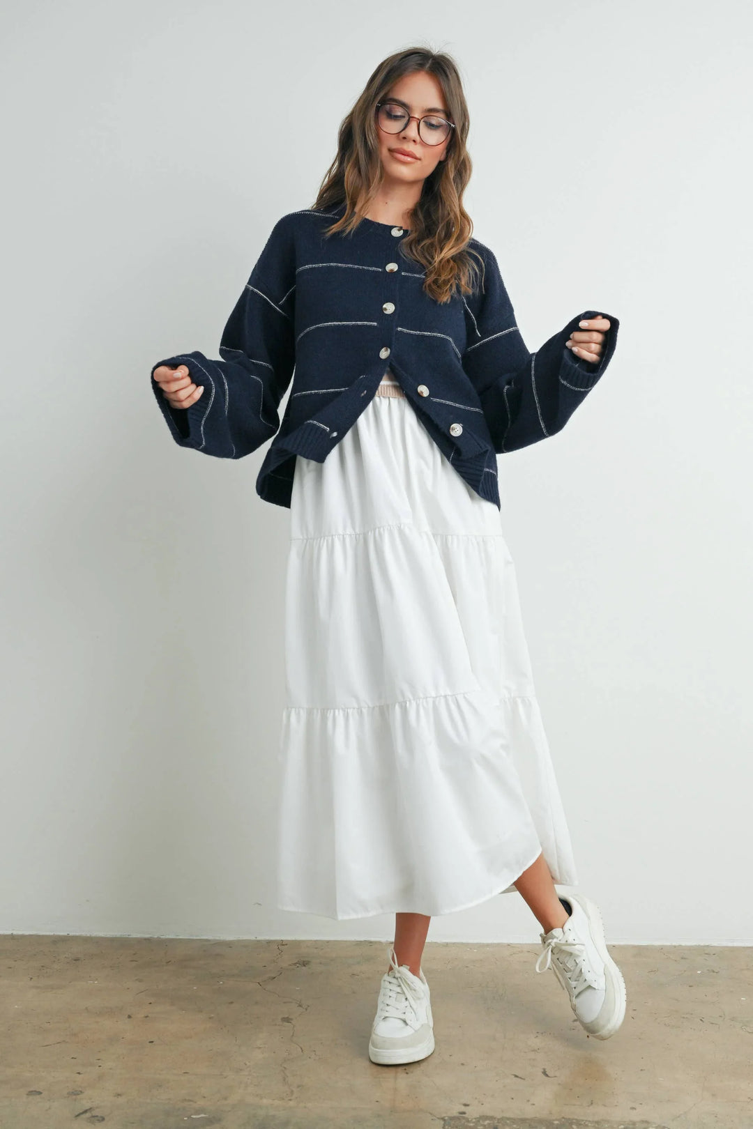 Navy cardigan with white stripes, layered over white tiered midi dress and white sneakers for coastal style