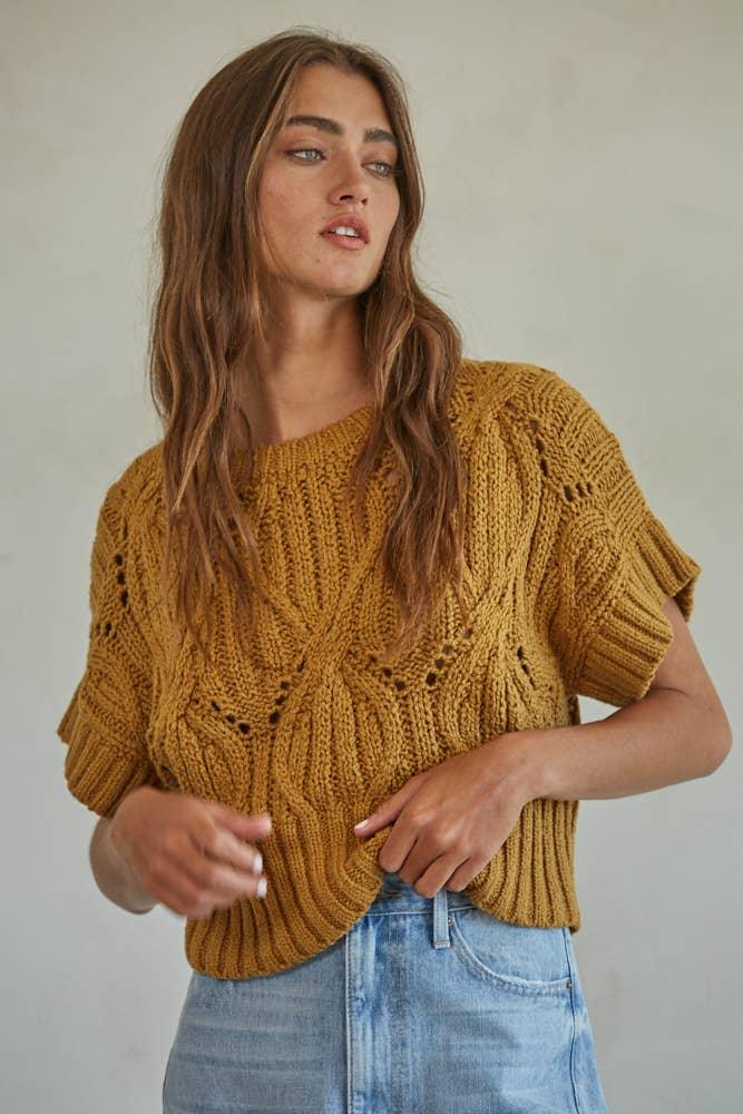 Mustard knit sweater with cable pattern, short sleeves, and relaxed fit paired with denim shorts