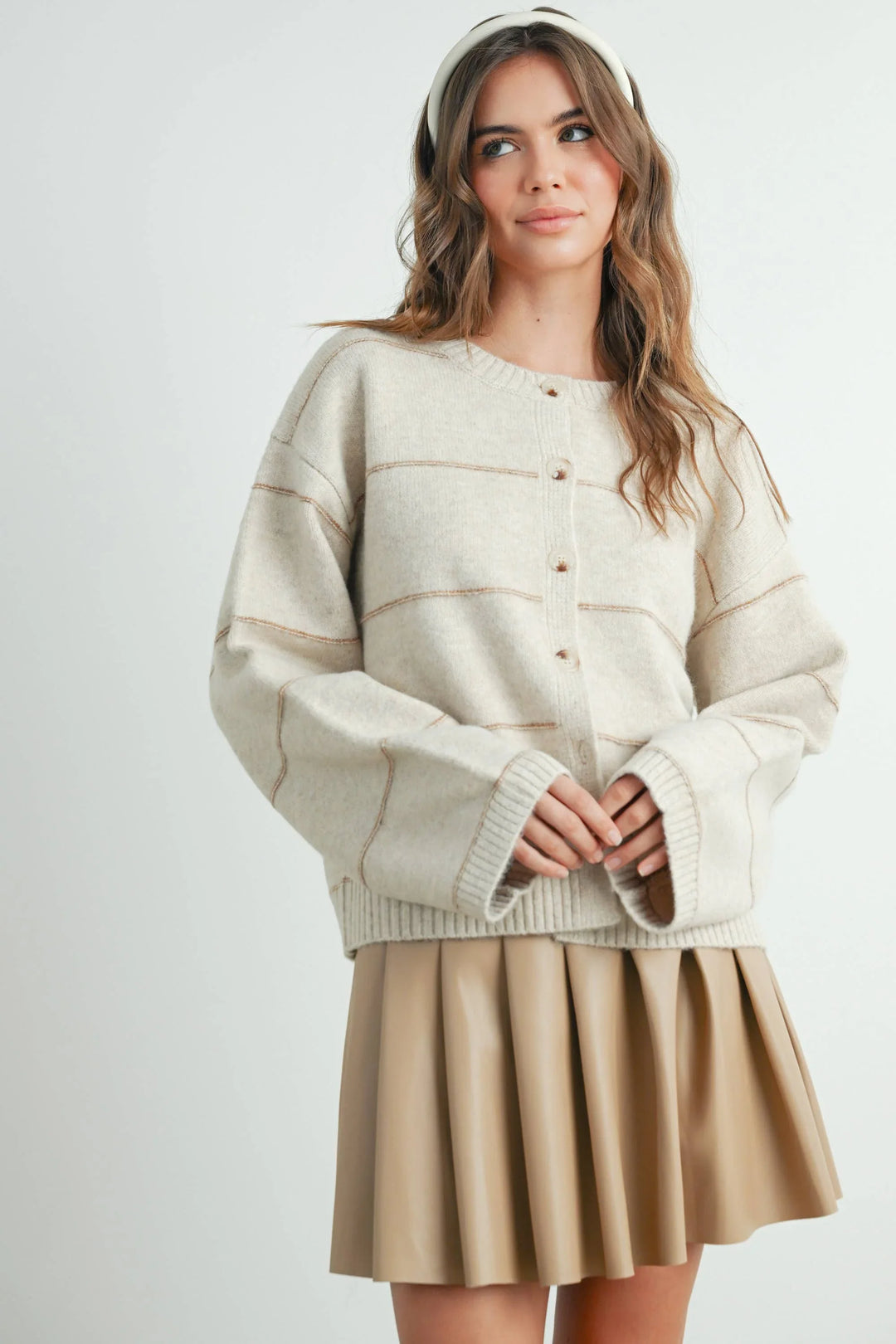 Cream button-front sweater with ribbed cuffs, paired with beige pleated mini skirt and white headband