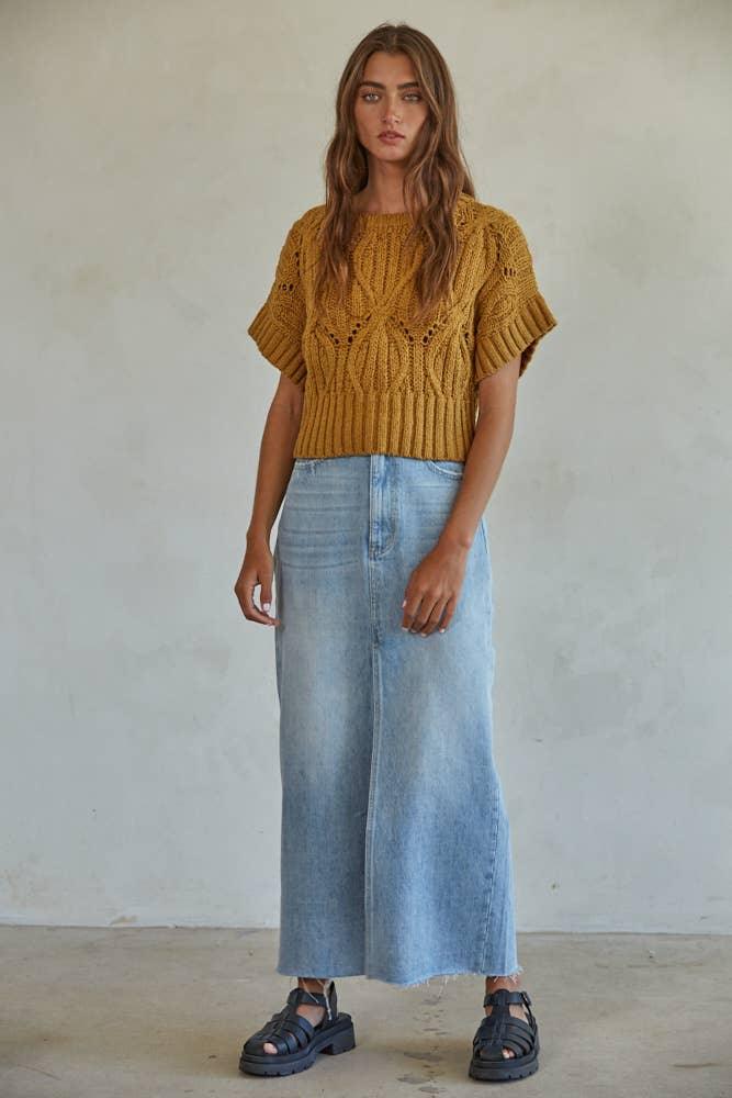 Woman in mustard knit crop top, light wash denim maxi skirt, and black sandals