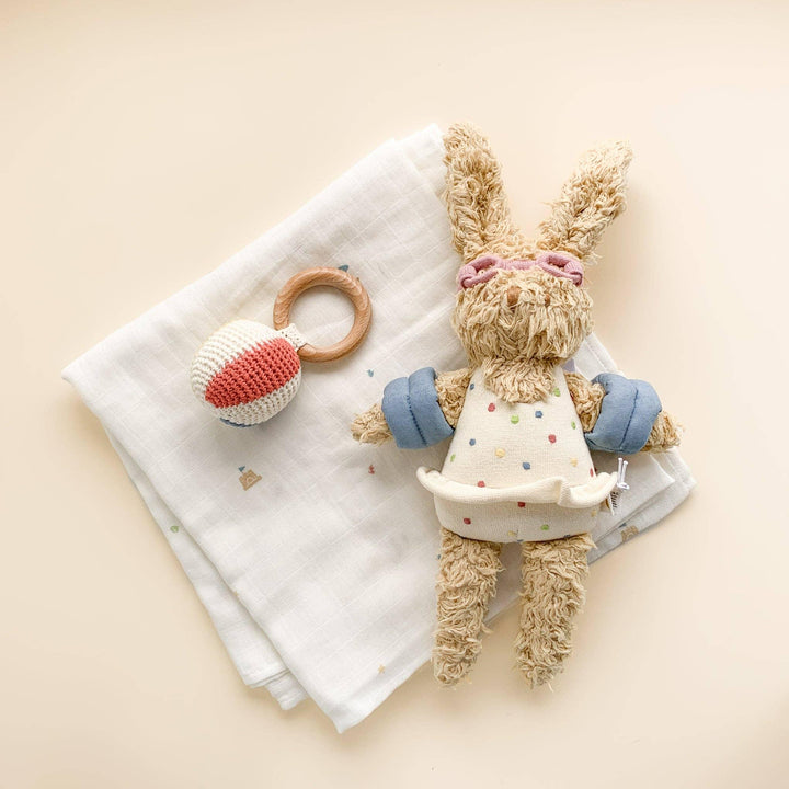 Soft bunny lovey with polka dot dress, wooden teether, and muslin blanket for baby comfort and play