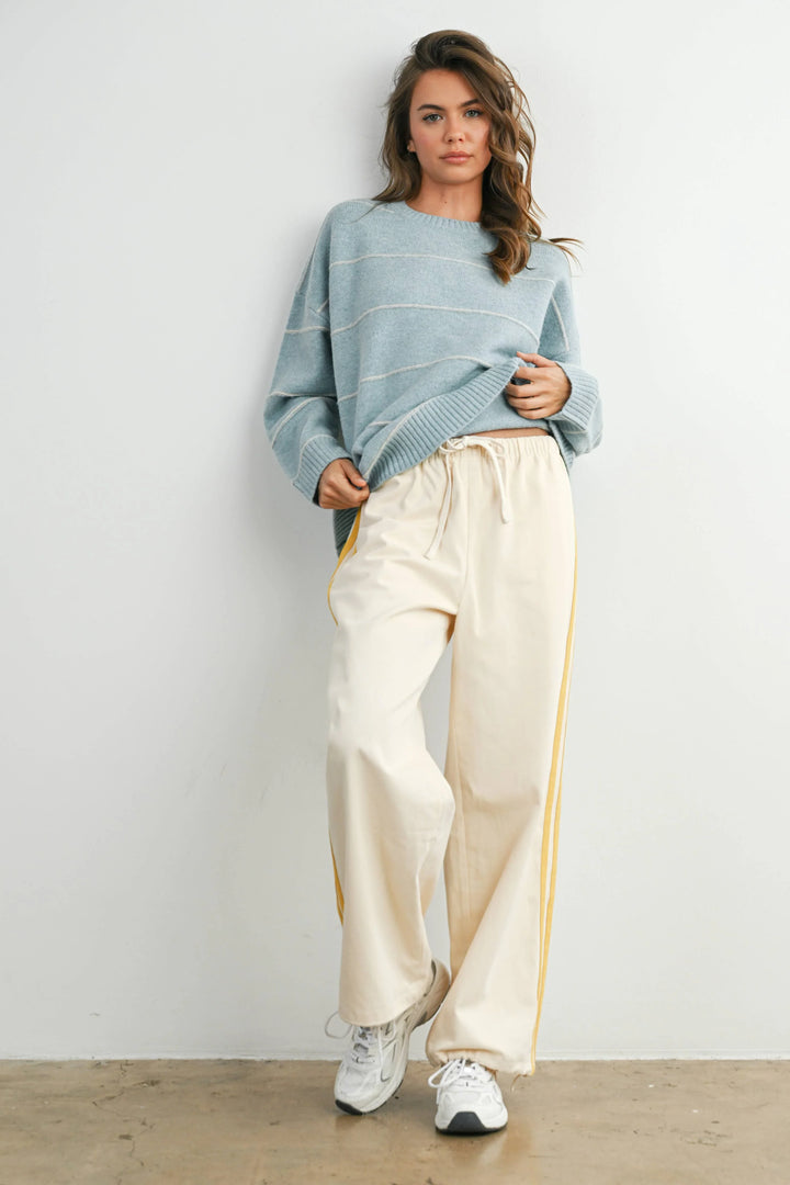 Woman in cozy blue striped sweater and cream wide-leg track pants with yellow side stripes, styled for PNW coastal comfort.