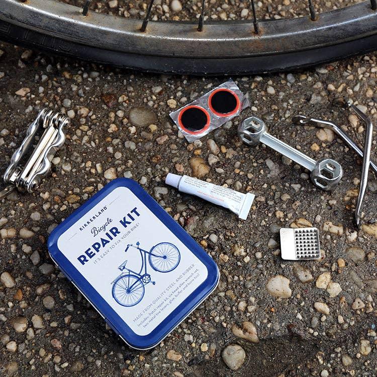 Compact bicycle repair kit with tools, patches, and tire levers on gravel near bike wheel