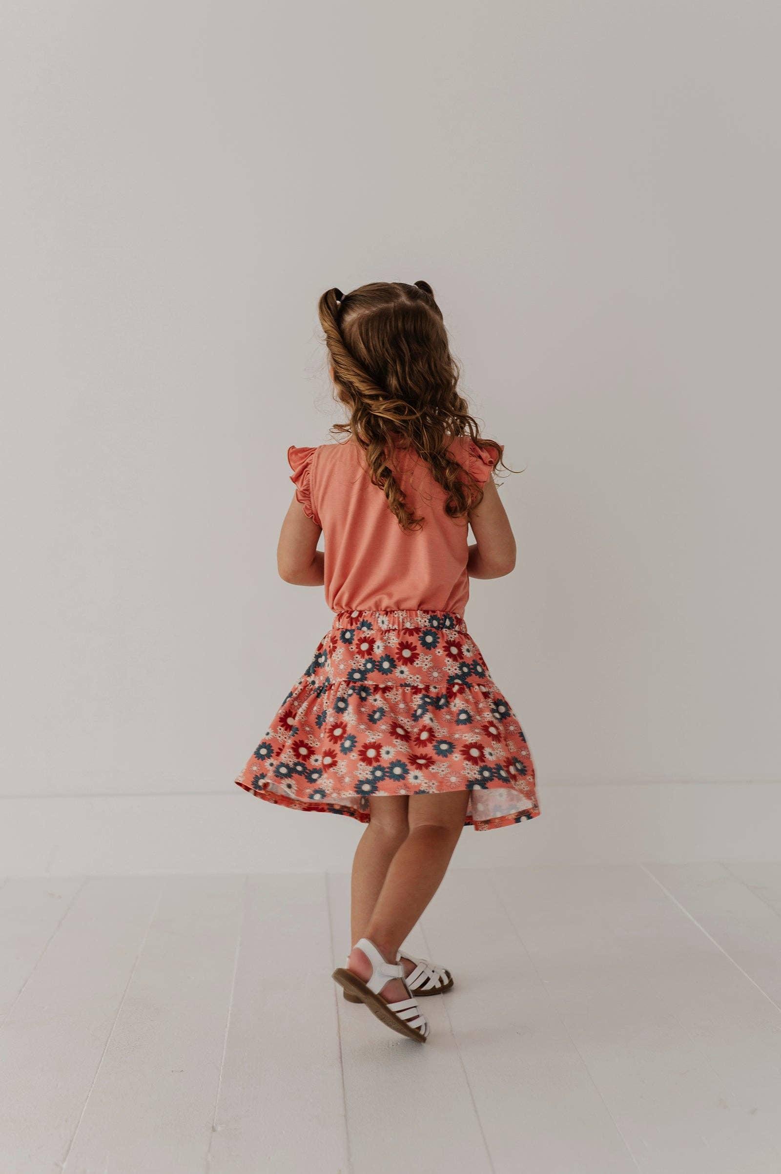 Toddler in coral floral dress with ruffle sleeves and white sandals, back view