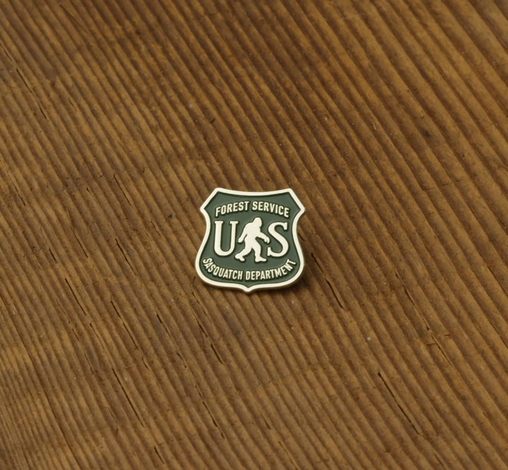 Forest Service Sasquatch Department enamel pin on wood