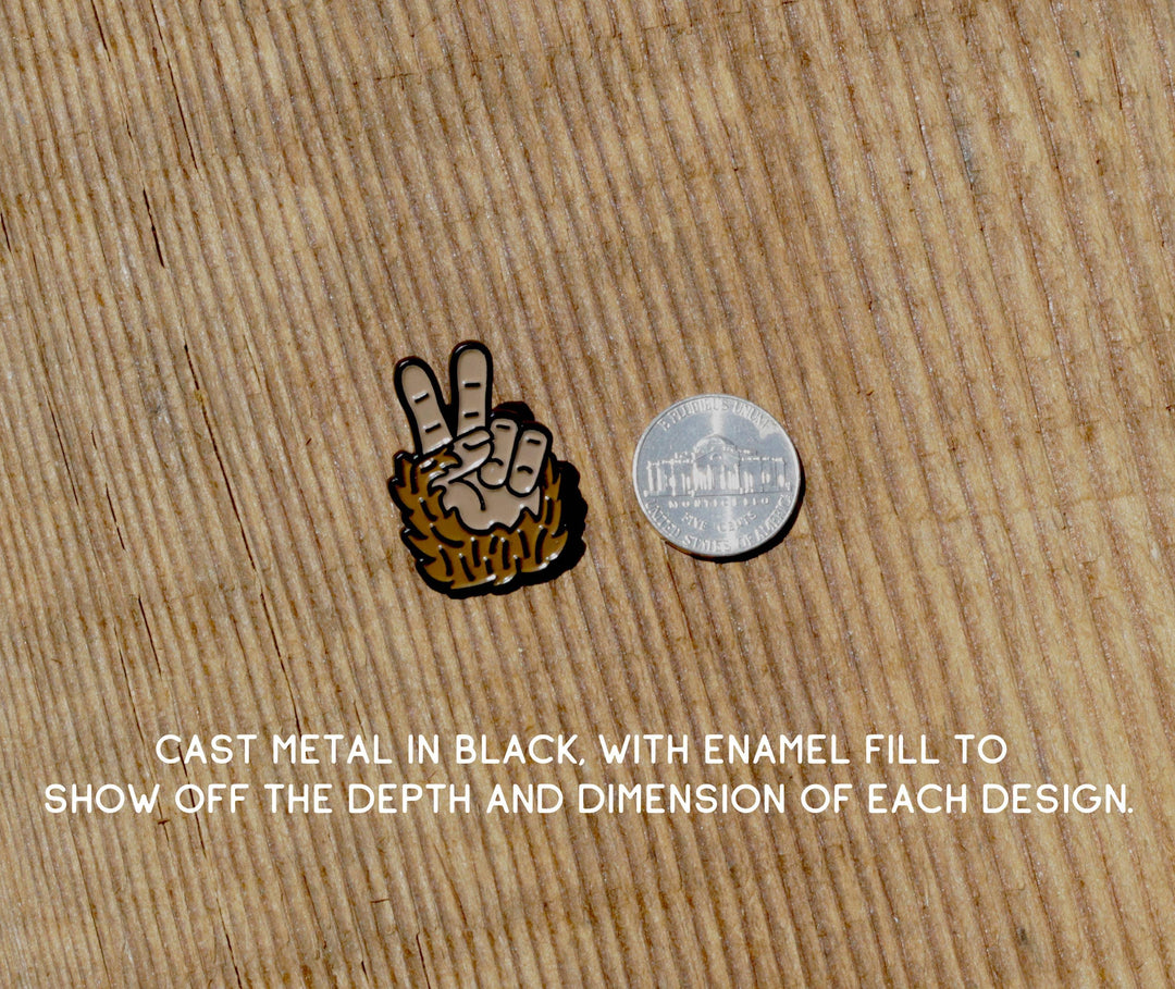Squatchy Bigfoot Peace enamel pin next to a US quarter on a textured wood background.