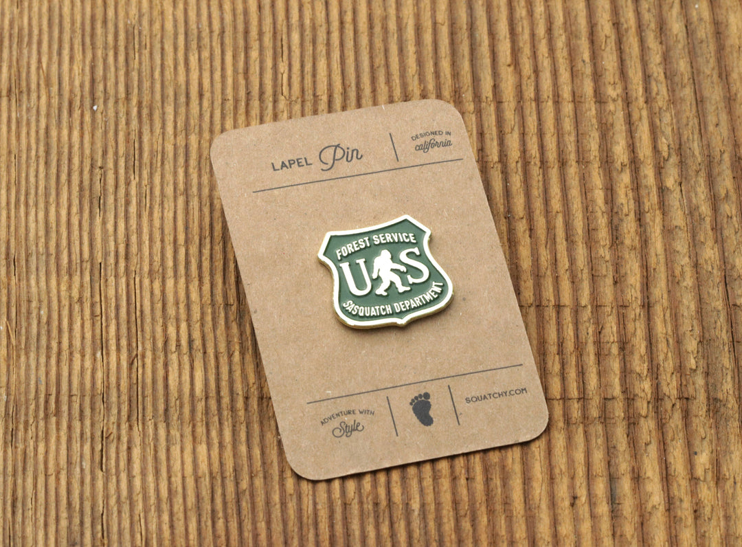 Forest Service US Sasquatch Department lapel pin on rustic wood background