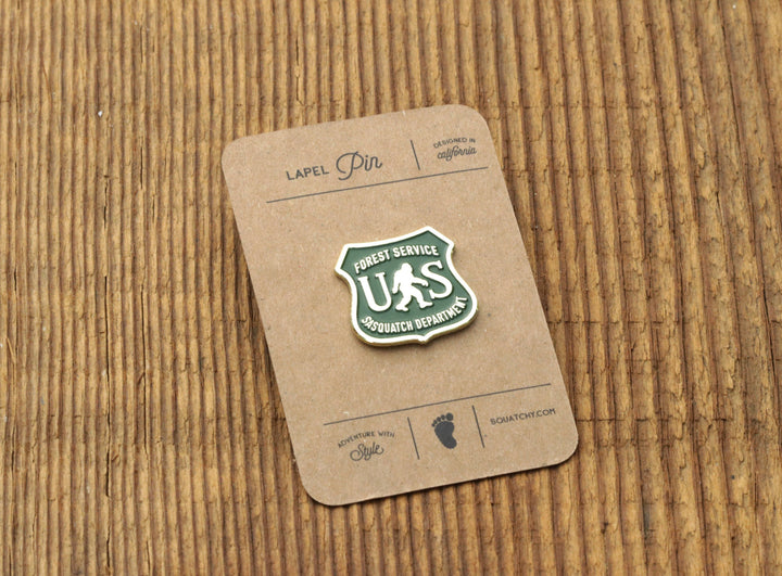 Forest Service US Sasquatch Department lapel pin on rustic wood background