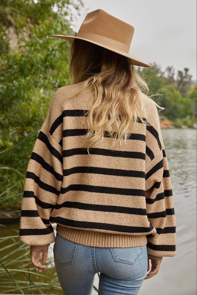Woman in striped sweater and wide-brim hat by lakeside, coastal outdoor style