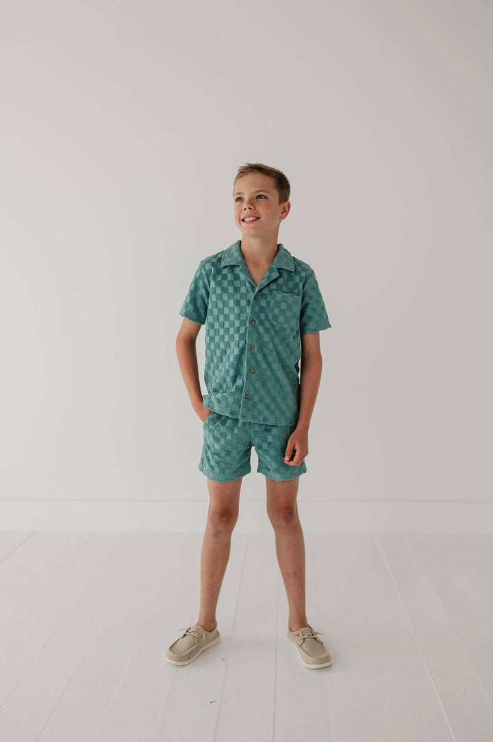 Boy in teal checkered short sleeve shirt and matching shorts, coastal style summer outfit