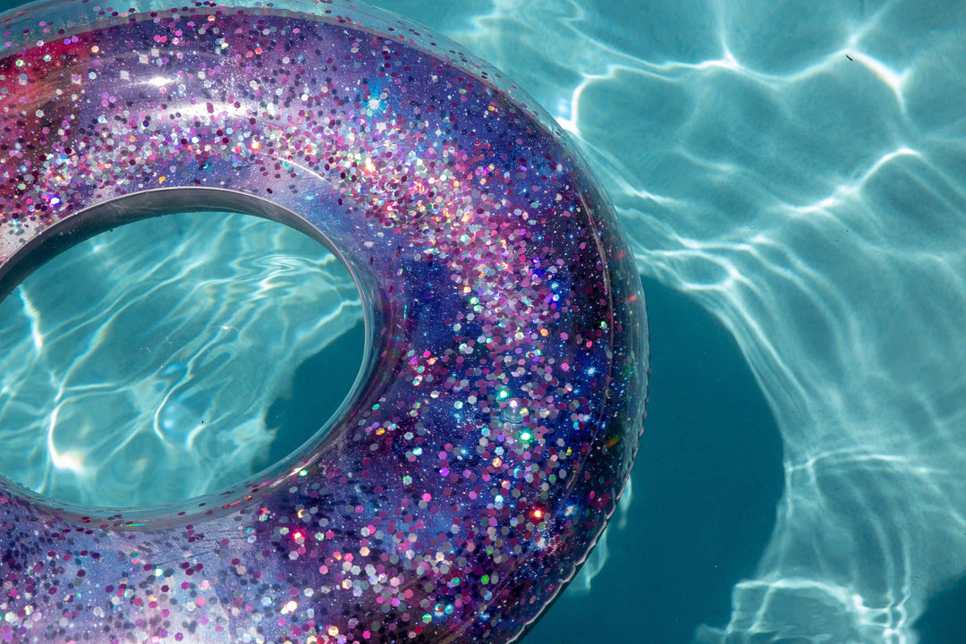 Glittery purple and pink pool float ring floating in clear blue water, perfect for beach days and summer adventures.