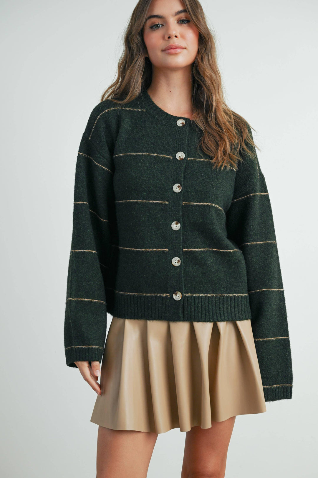 Woman in cozy green striped cardigan with buttons, paired with tan pleated skirt for casual coastal style.
