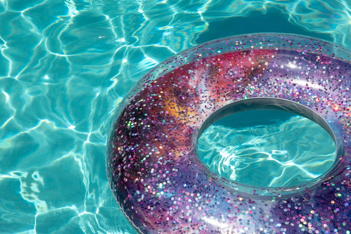 Glittery galaxy pool float in clear blue water, perfect for summer beach days and outdoor fun.