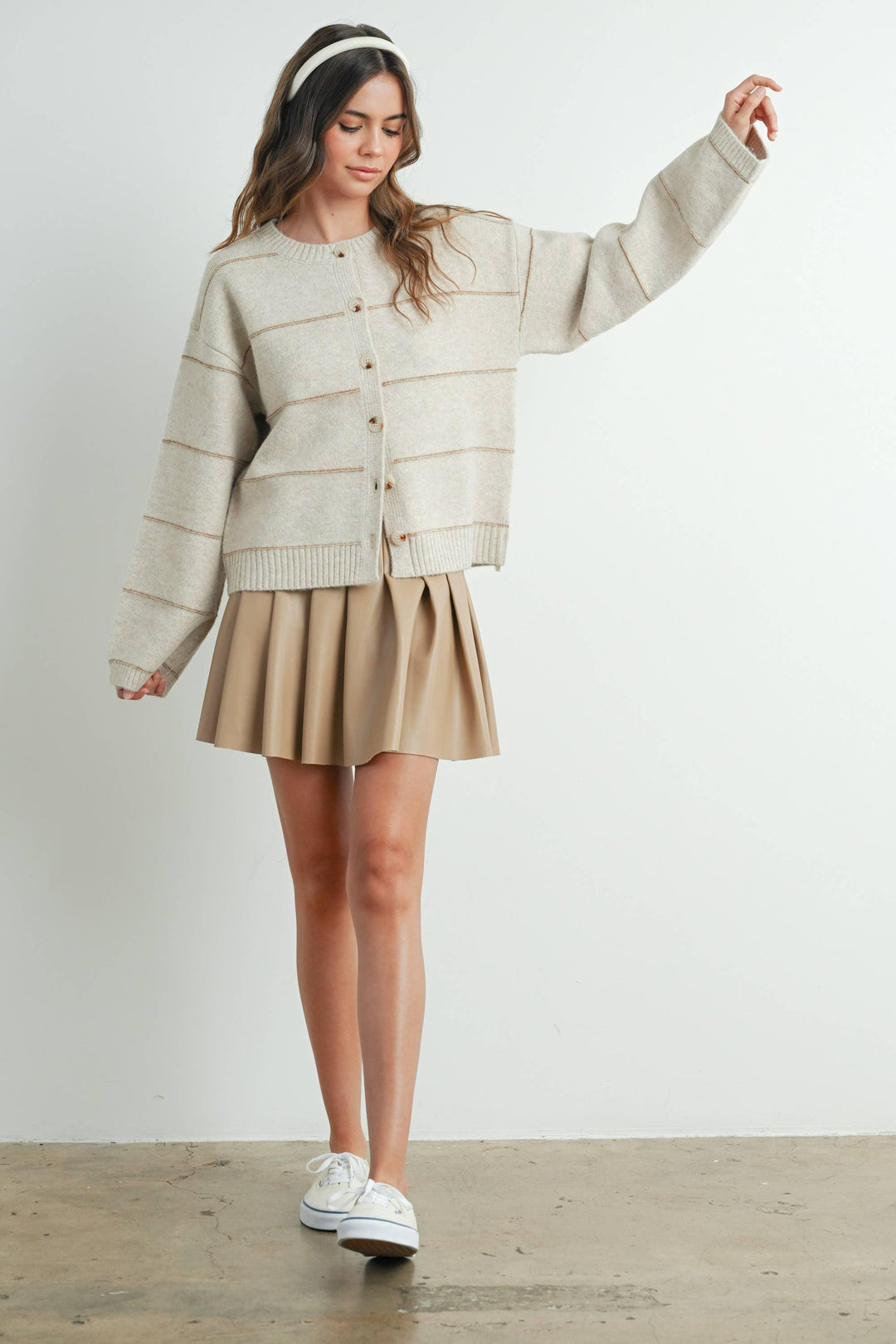 Cream button-up cardigan with ribbed trim, paired with pleated skirt and white sneakers for casual coastal style