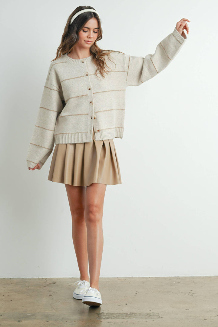 Cream button-up cardigan with ribbed trim, paired with pleated skirt and white sneakers for casual coastal style