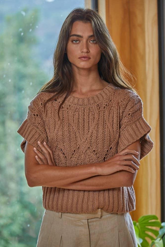 Woman wearing cozy brown knit sweater with short sleeves and ribbed hem, standing by window